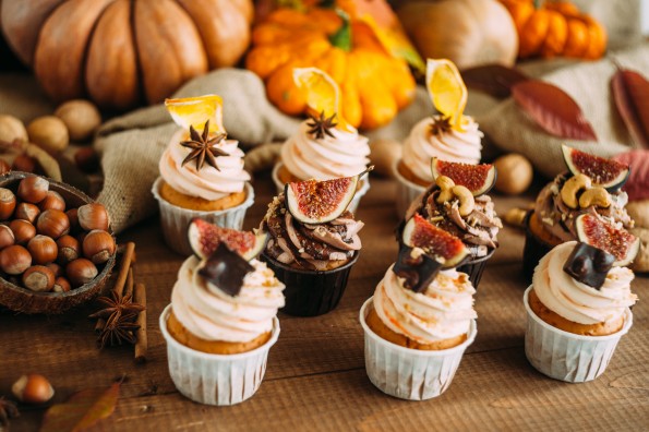 Autumn tasty cupcakes on a wooden background with autumn harvest. Pumpkins, patches, apples, nuts, spices.